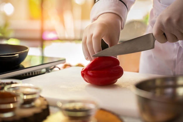 Hand with knife cuts pepper. Red paprika on cooking board. Fresh vegetable for a salad. Chef of cafe is busy.