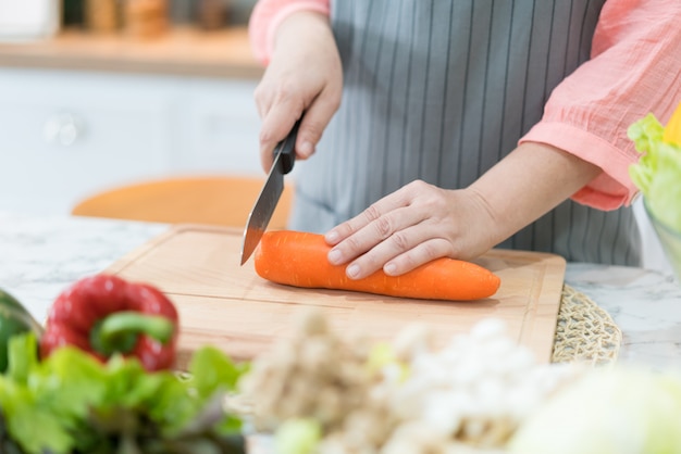 Hand with knife cutting carrot. Woman prepares food at table.