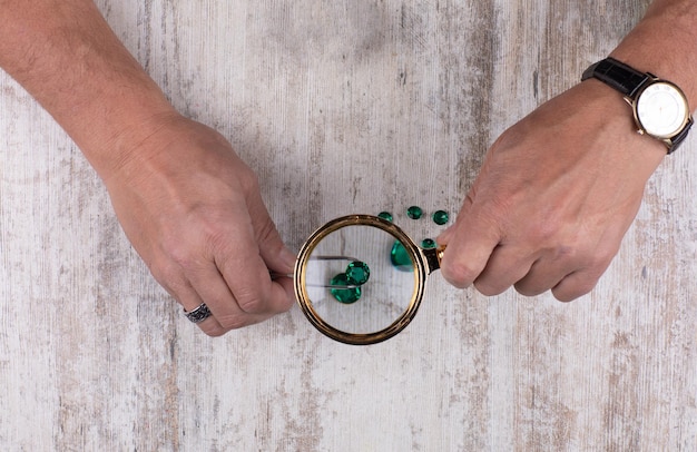 hand with a magnifying glass looks at the emerald