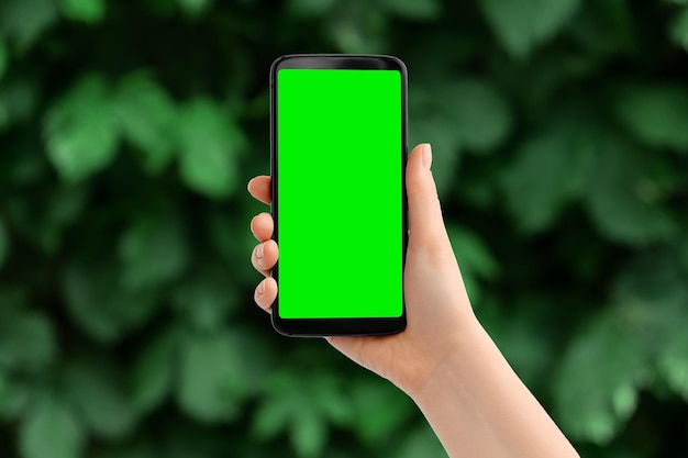 Hand with the phone upright against blurred greens Smartphone with a green screen copy space