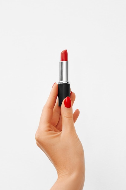 The hand with red manicure holds a bright red lipstick on white background