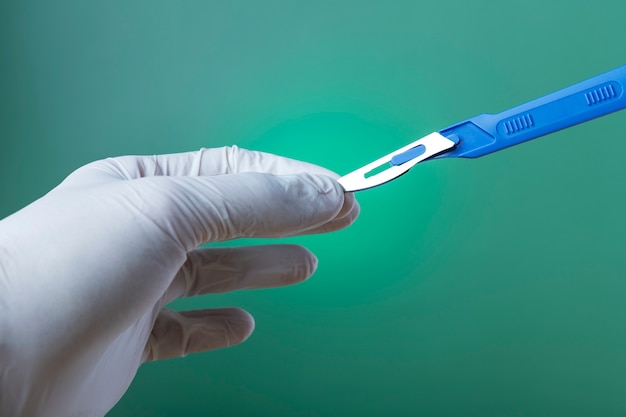 Photo hand with rubber glove holding medical scalpel