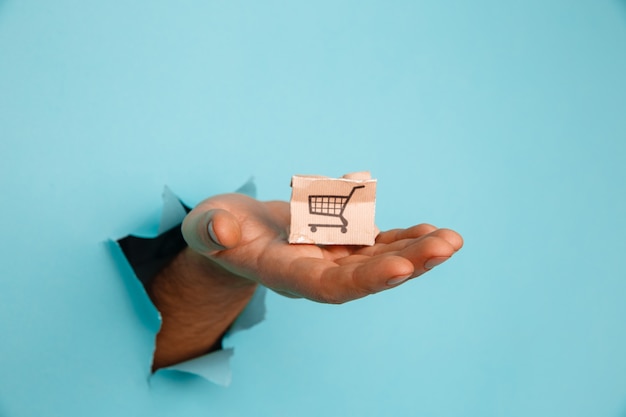 Hand with a small delivery box through a blue paper hole.