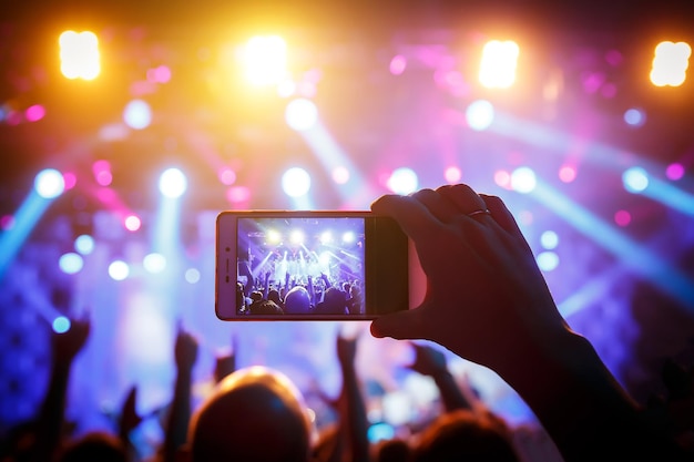 Hand with a smartphone records live music festival and taking photo of concert stage