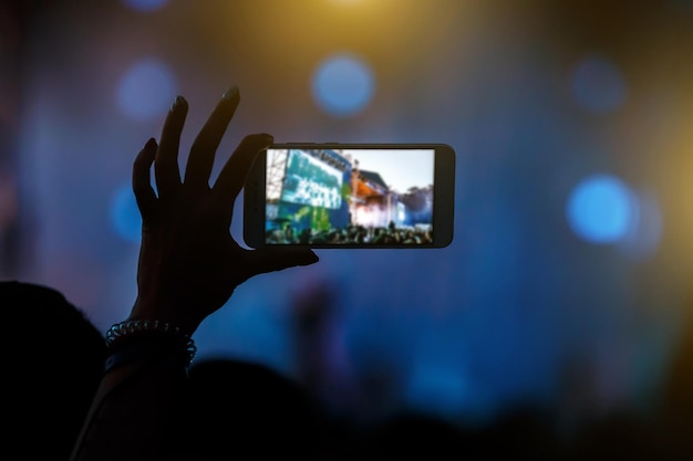 Hand with a smartphone records live music festival and taking photo of concert stage