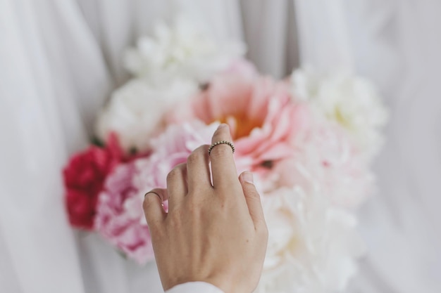 Hand with stylish rings on beautiful peonies bouquet Tender image Feminine essentials