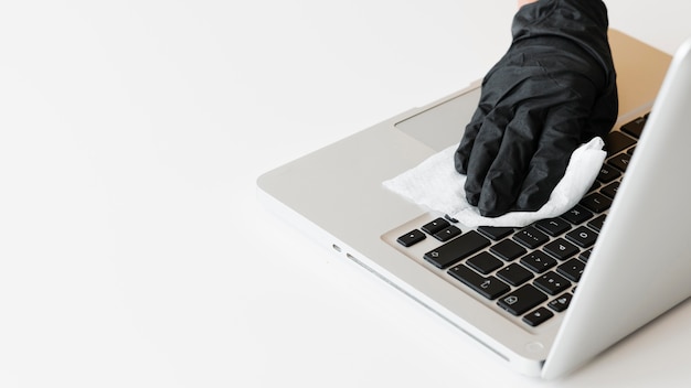 Hand with surgical glove disinfecting laptop with copy space