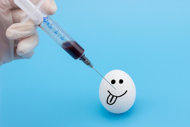 A hand with a syringe makes an injection into the egg closeup The concept of GMO in products