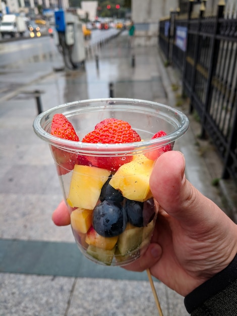 Hand with transparent plastic cup of sliced fruits