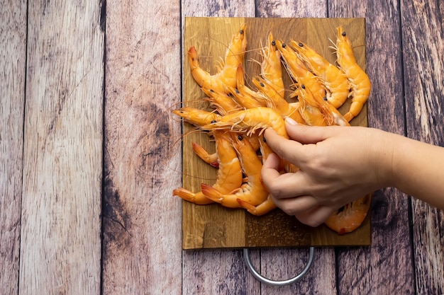 A hand with two fingers holds a shrimp against the background of a wooden stand with shrimp