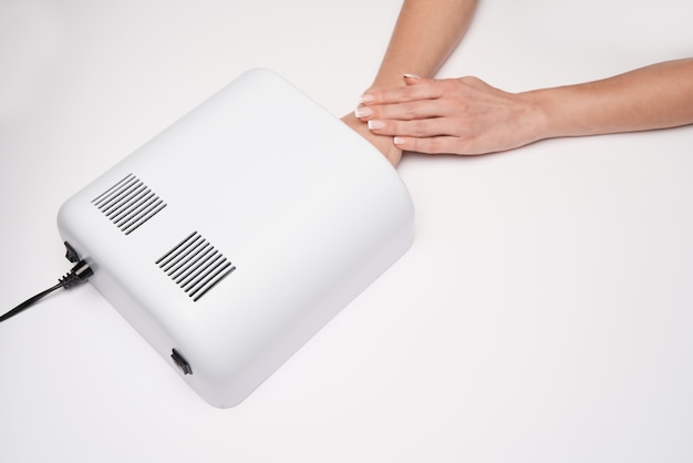 Hand with UV timer lamp lights for nails over light surface