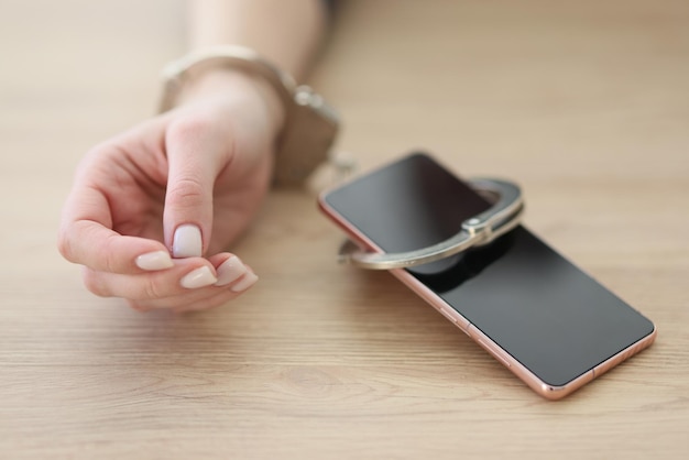 Hand of woman attached to smartphone with handcuffs on wooden table dependency and addiction to