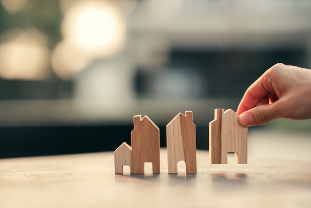 Hand of woman choosing mini wood house model, Planning buy Real Estate, eco house icon concept.