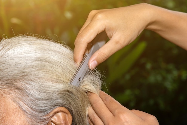 Hand of woman cutting her elderly mother's hair in nature at home