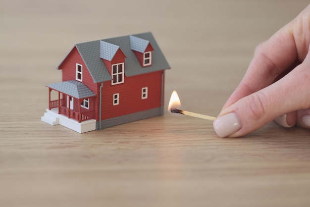 Hand of woman holding match to burn house on wooden table