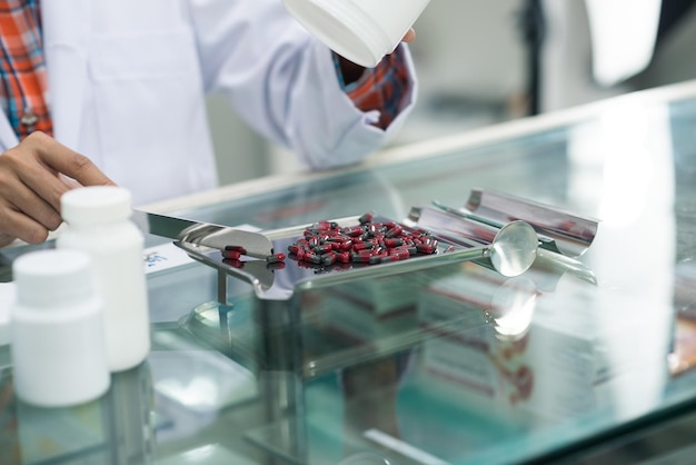 Hand of woman pharmacist pour and count drug capsules on stainless tray, she prepare drug pack to patient in the pharmacy drugstore. Healthy and medicine concept.