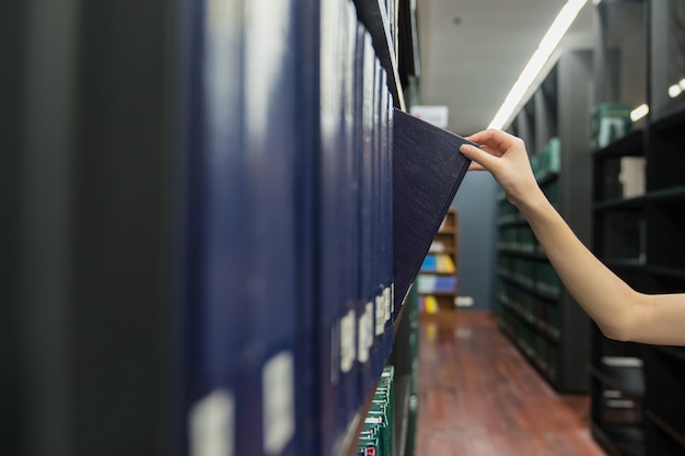 Hand of woman pulling a Thesis book off the shelf in Library. Green colors books.