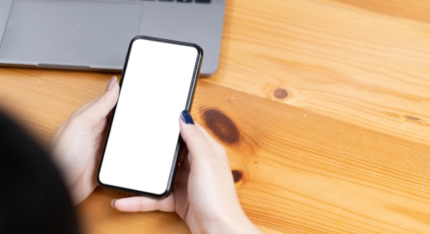 Hand woman using a telephone empty screen smart phone and computer on wooden table top view