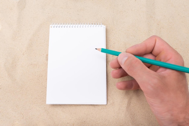 Hand writes on a white sheet on a sandy background layout template