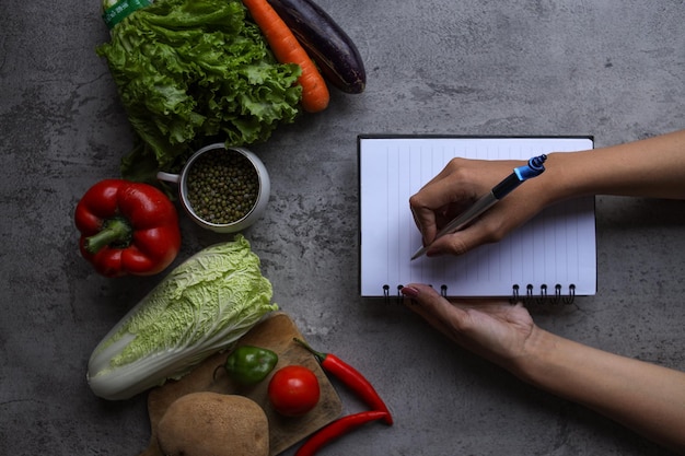 hand writing recipes on book with food ingredients and fresh vegetables in the kitchen