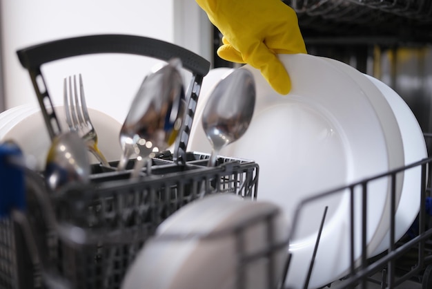 A hand in a yellow glove pulls dishes out of the dishwasher