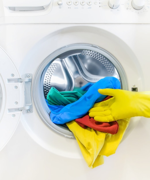 Hand in a yellow glove takes the color Laundry out of the washing machine