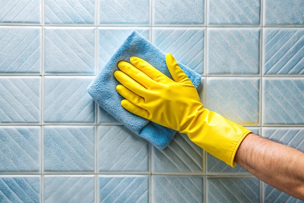 Photo hand in yellow protective glove cleaning tiles with rag