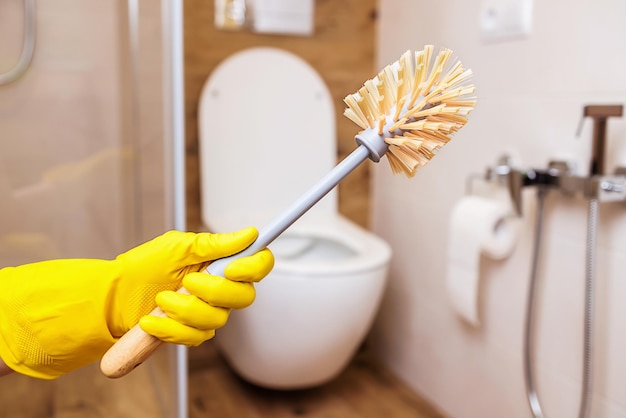 Hand in yellow rubber glove holds toilet brush on the background of the bathroom