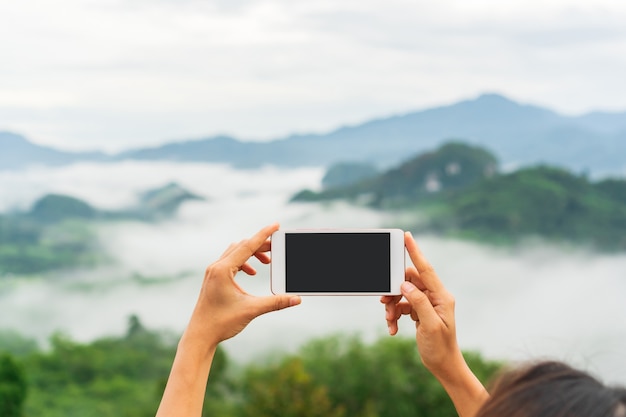 Hand young Asian traveler woman  using smartphone take a photo on mountain. Close up, copy space