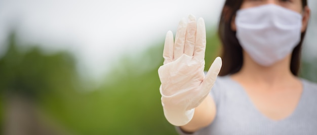 Photo hand of young asian woman with gloves showing stop gesture while wearing mask for protection from corona virus outbreak