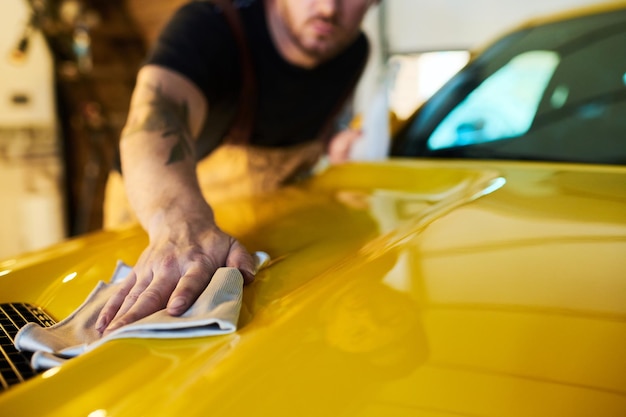 Hand of young male technician with duster wiping surface of yellow car body