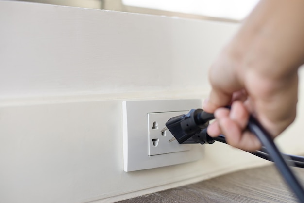 In the hand of a young man holding a power cord to unplug unused appliances to save energy save money