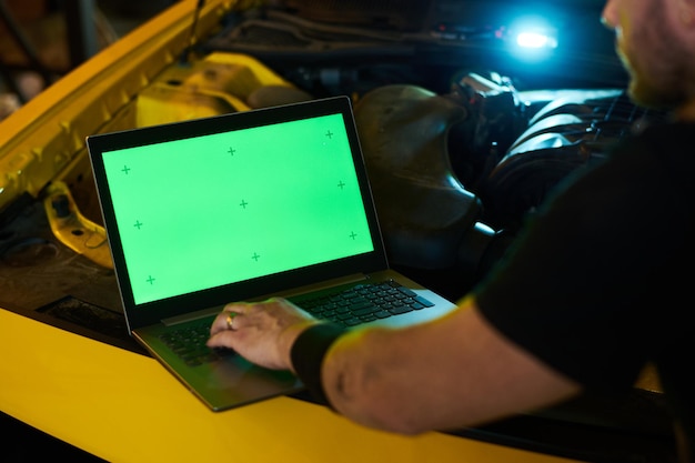 Hand of young mechanic or repairman on keypad of laptop with green screen