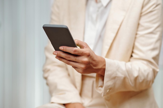 Hand of young woman in beige blazer texting in mobile phone