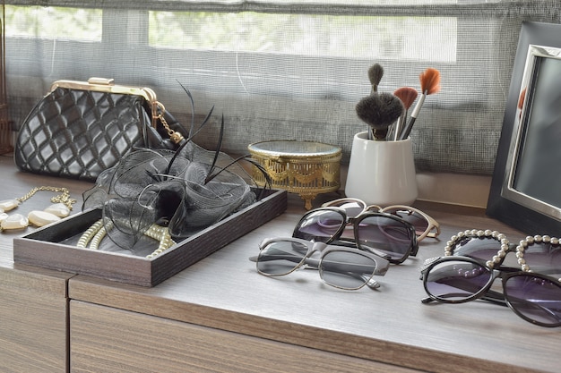 Handbag,sunglasses,jewelry and makeup brushes on a wooden dressing table 