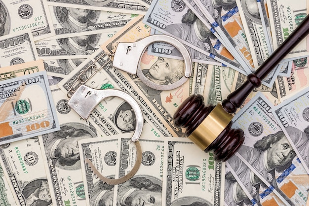 Handcuffs and judge gavel on dollar banknotes surface