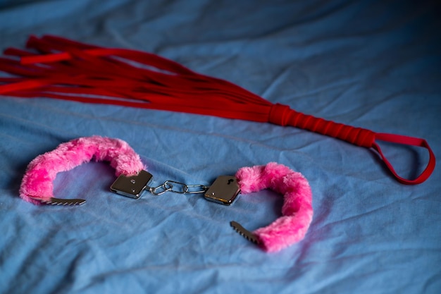 Handcuffs with red fur and a whip Devices for love games on the bed