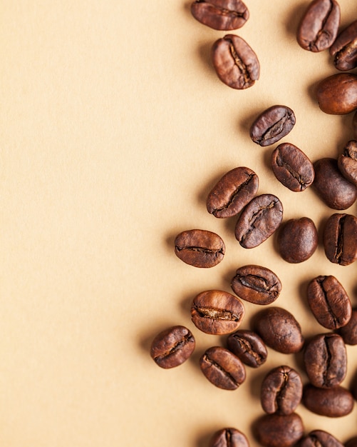 A handful of arabica coffee beans on a light brown background. Vertical photo with place for text for coffee houses, screensavers, roasters and coffee makers.