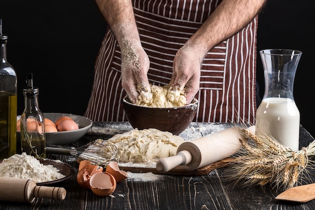 A handful of flour with egg on a rustic kitchen. Against the background of men's hands knead the dough. Ingredients for cooking flour products or dough bread, muffins, pie, pizza dough . Copy space