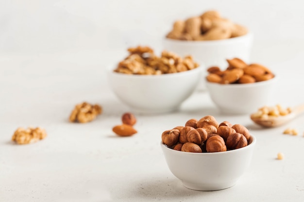 A handful of hazelnuts in a white bowl, assorted nuts on a light background. Healthy snacks, healthy fats. Copy space.