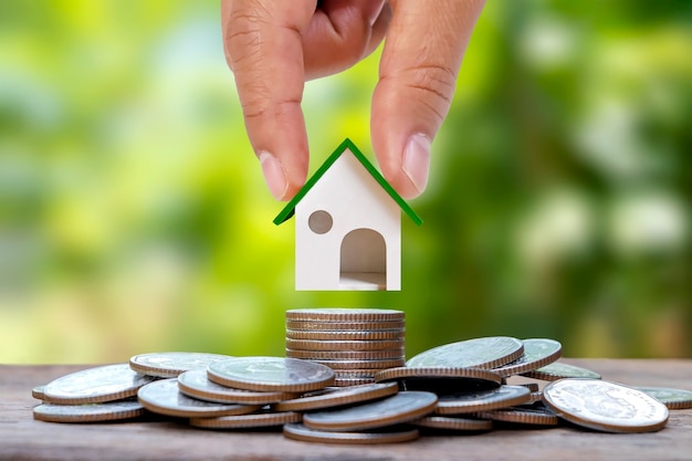 Handholding model house on a pile of coins with blur green natural background home loan