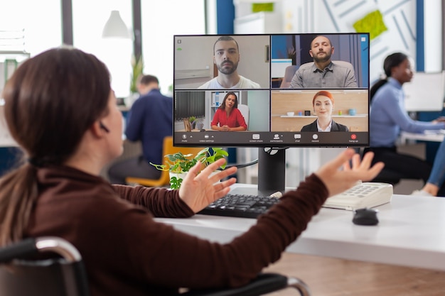 Handicapped amputee paralysed project manager talking with team during video conference using videoc...