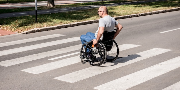 Handicapped man in wheelchair crossing street road.