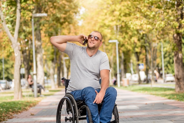 Handicapped man in wheelchair at the park alley use a smartphone