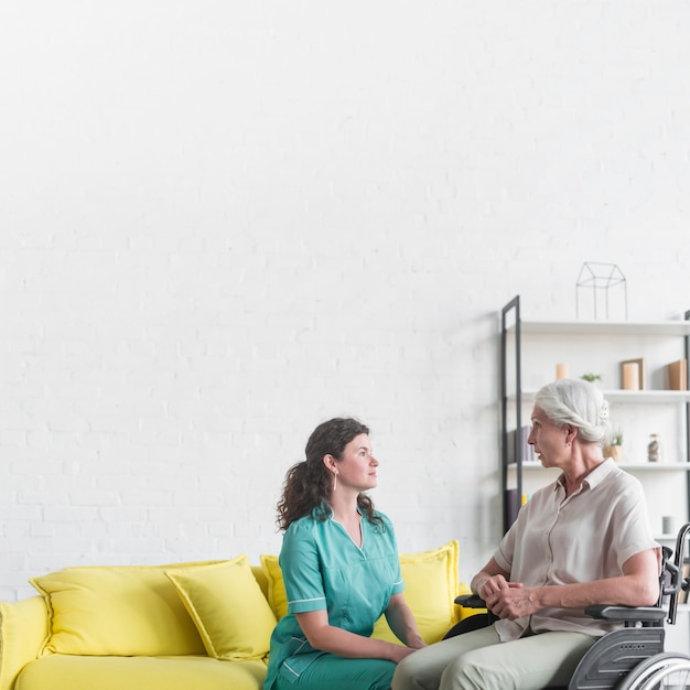 Handicapped senior woman sitting on wheel chair looking at nurse