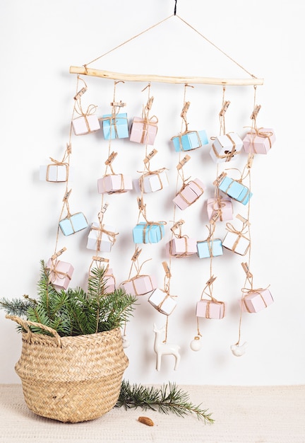 Handmade advent calendar with gift boxes hanging on ropes and pine needles in wicker basket