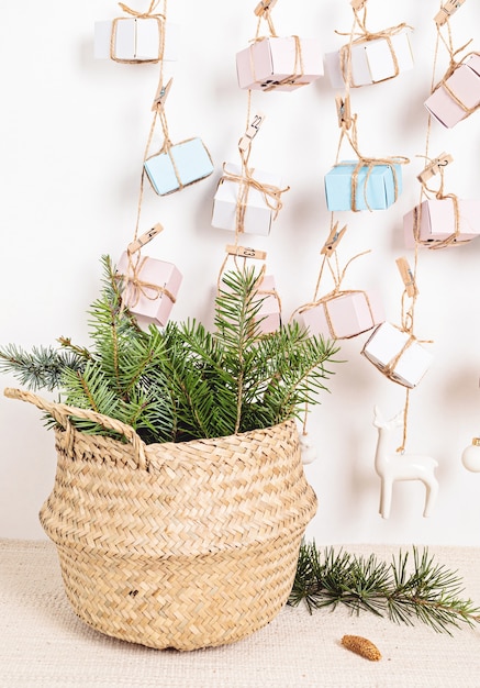 Handmade advent calendar with gift boxes hanging on ropes and pine needles in wicker basket