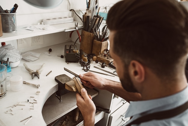 Handmade. Back view of young male jeweler making a ring at his workbench. Jewelry making process. Jewelry equipment. Working process. Jewelry manufacturing concept.