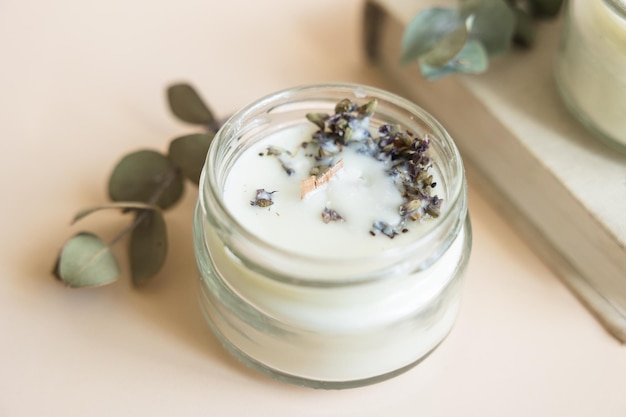 Handmade candle from paraffin and soy wax in glass with wooden wick and dry herbal isolated on pastel beige background Flat lay top view copy space