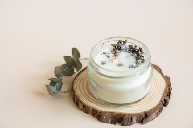 Handmade candle from paraffin and soy wax in glass with wooden wick and dry herbal isolated on pastel beige background Flat lay top view copy space